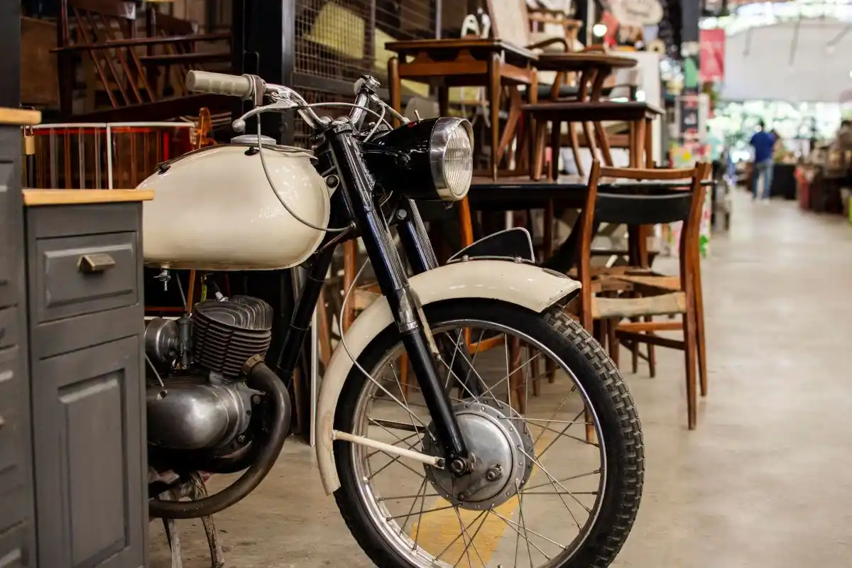 Altes beiges Motorrad steht zwischen Stühlen und Vitrine in einer Halle