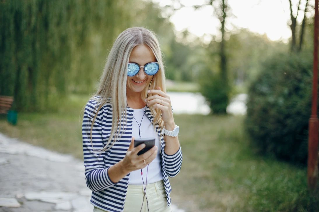 Lächelnde Frau mit Sonnenbrille tippt auf ihrem Handy