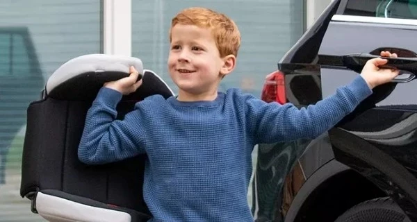 Rothaariger-Junge-mit-Sitzerhöhung-vor-schwarzem-Autp