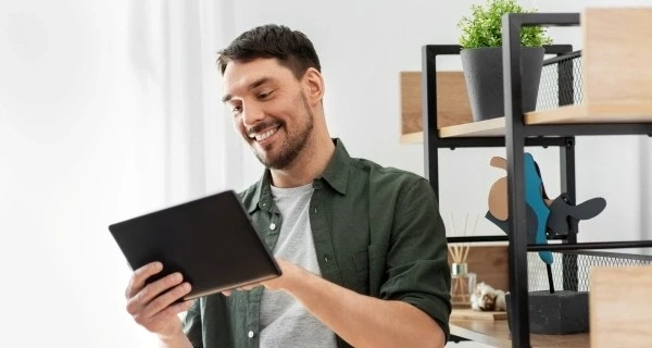 glücklicher-lächelnder-Mann-mit-Tablet-PC-Regal-Zuhause
