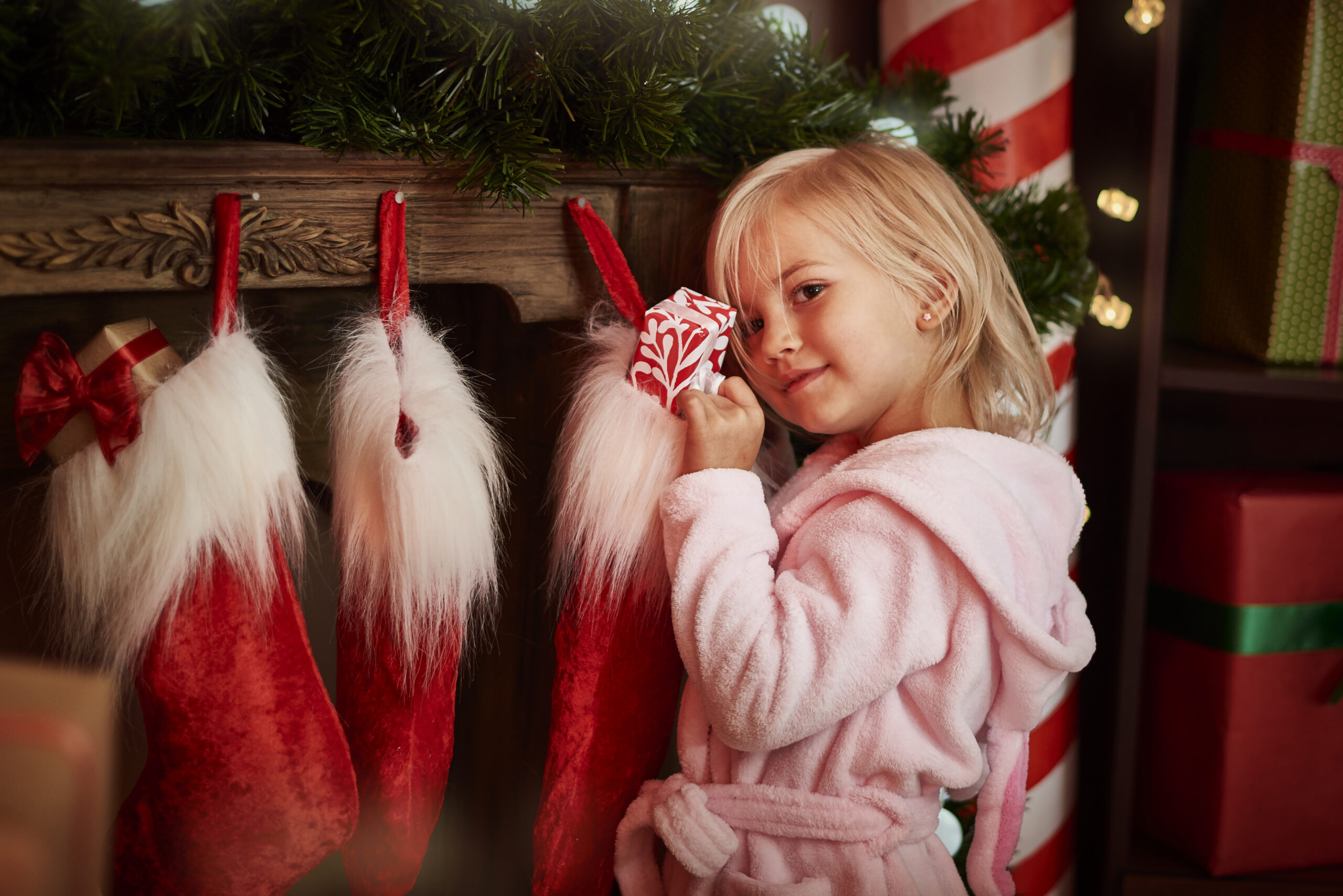 Kleines Kind mit blonden Haaren steht lächelnd an einem roten Nikolausstiefel