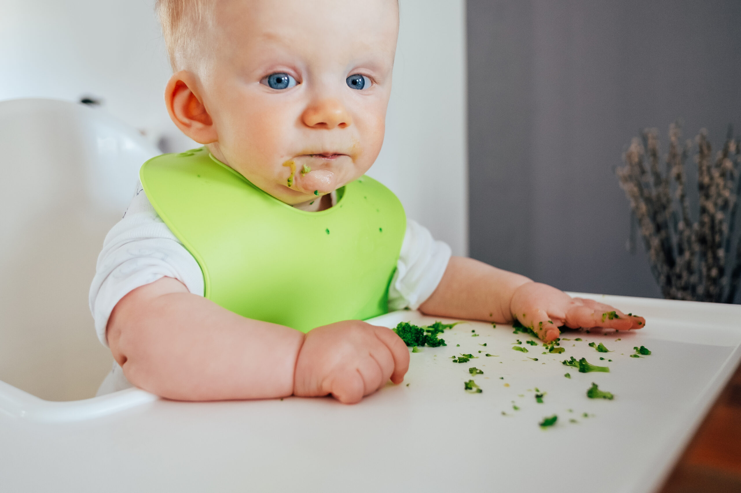 Blondes Kleinkind mit grünem Lätzchen beim Essen und Kleckern