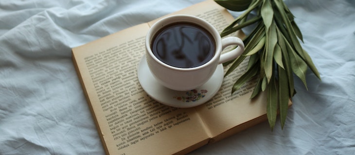 Schwarzer Tee in Tasse mit Unterteller steht auf offenem Buch