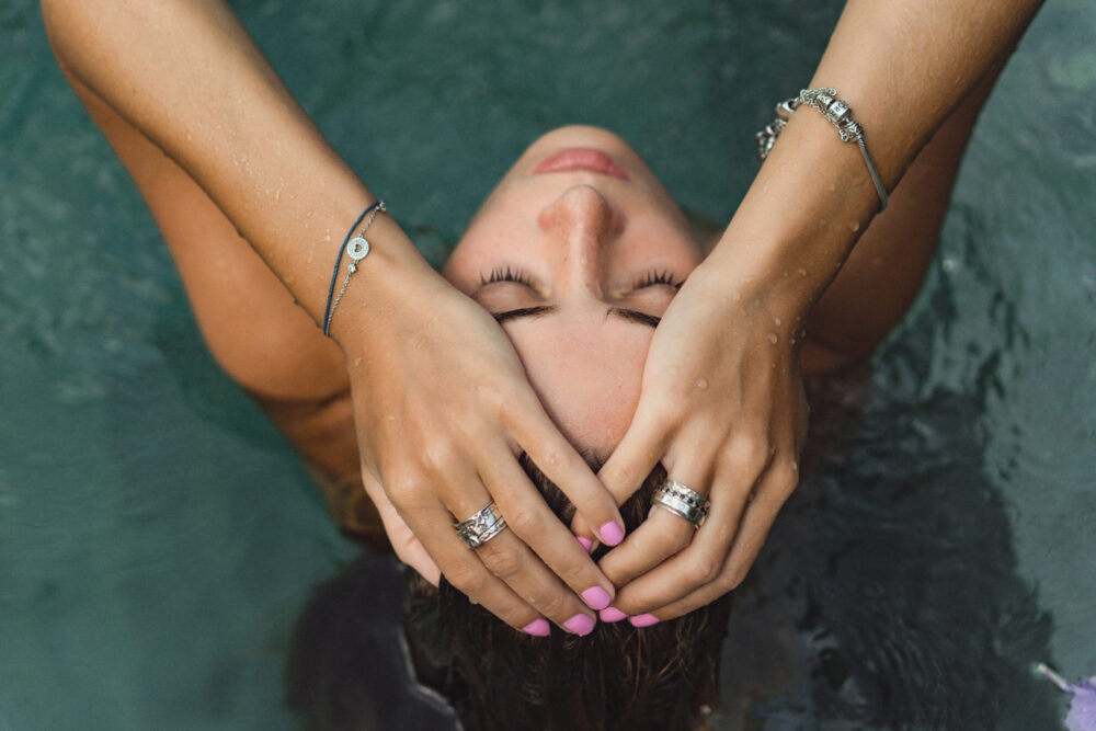 Frau mit Goldschmuck am Handgelenk unter fließendem Wasser